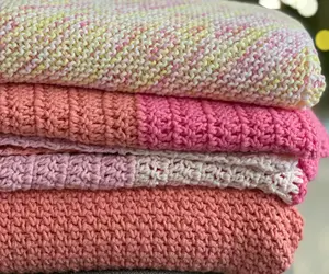 A pile of four knit blankets in various yarns and colors