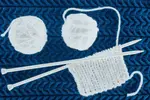 Balls of white yarn, needles and work on a blue background