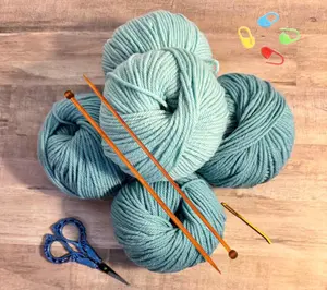 A knitting kit for beginners showing yarn, needles, scissors, and stitch markers