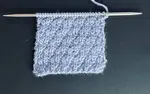 The seersucker knit stitch pattern worked in blue wool yarn