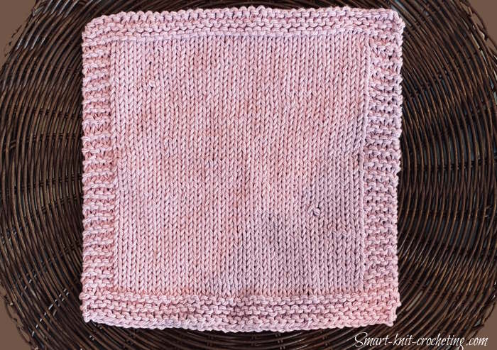 Stockinette stitch dishcloth with a garter stitch border knit in a pink cotton yarn.