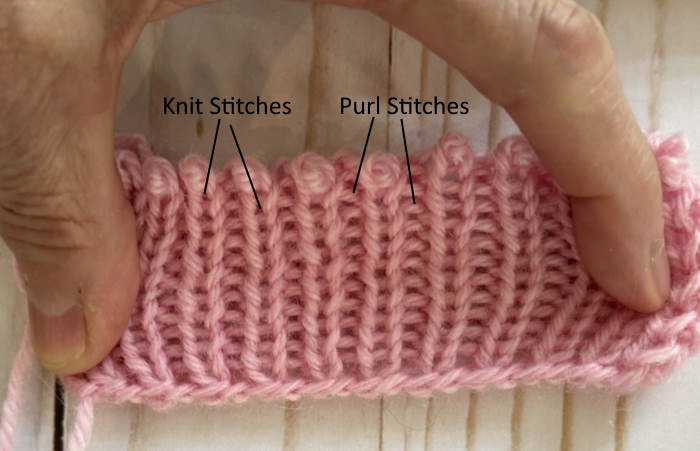 1 x 1 Ribbing Stretched to See Stitches A swatch of 1 x 1 ribbing in pink yarn stretched to show knit and purl stitches