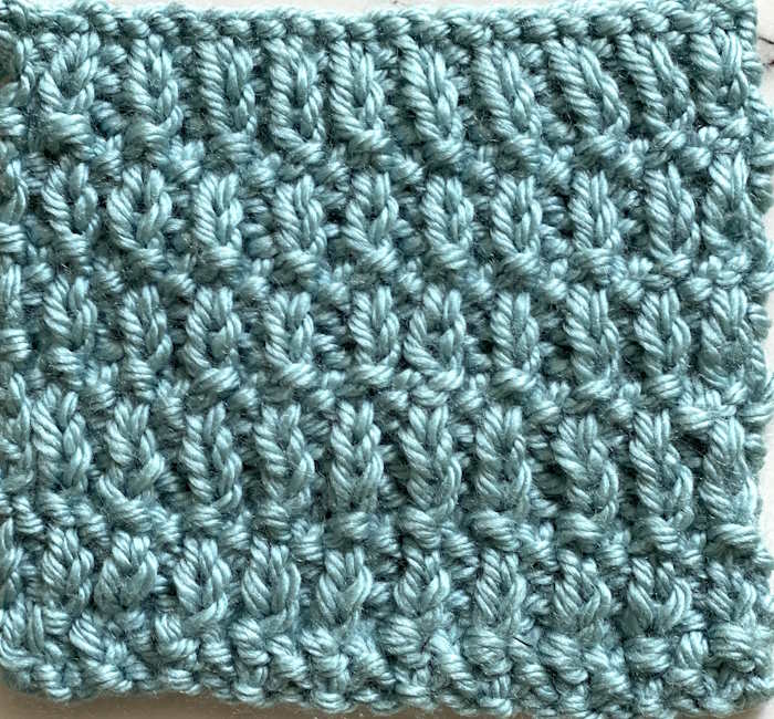 The bumpy knit stitch swatch is worked in an acrylic worsted weight yarn in the color teal. The bumpy knit stitch swatch is worked in an acrylic worsted weight yarn in the color teal.