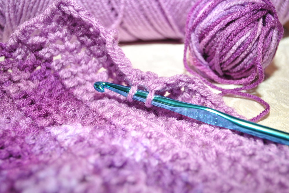 Purple yarn, a crochet hook, and a swatch of crochet fabric