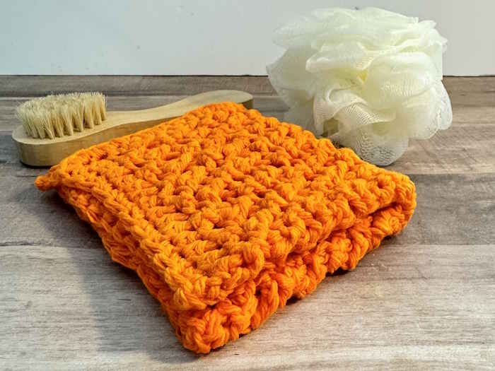 A washcloth made with the crossed half-double crochet stitch in orange 100% cotton. A washcloth made with the crossed half-double crochet stitch in orange 100% cotton.