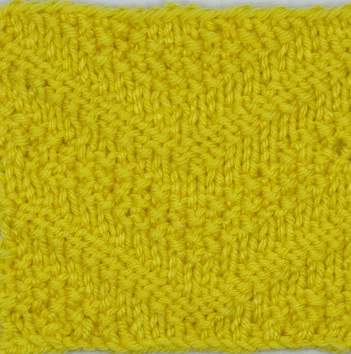 A knitted swatch of the seed stitch chevron stitch pattern worked in yellow
