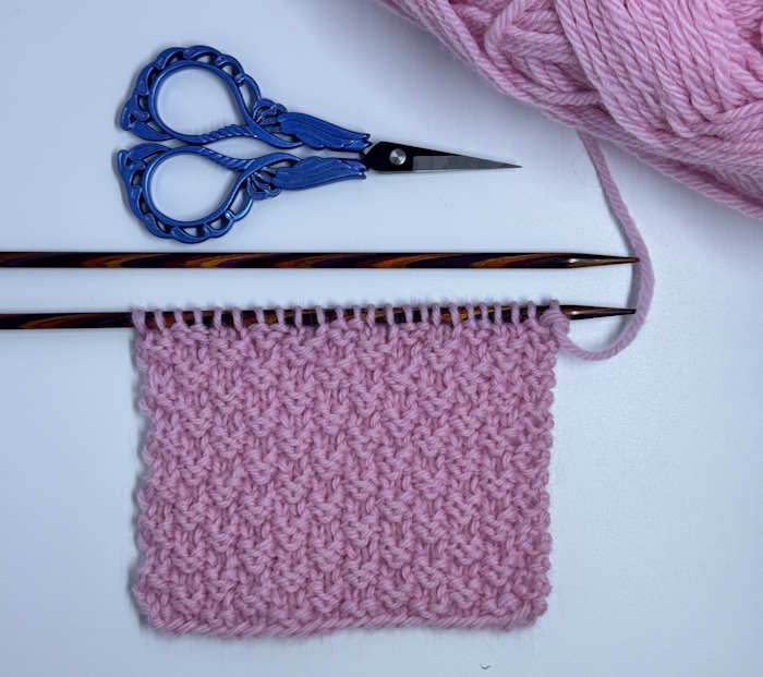 Double Moss Stitch Double moss stitch swatch on needles worked in pink yarn.