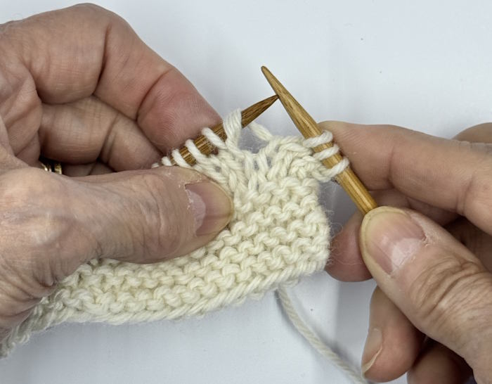 A swatch still on the knitting needles demonstrating how to make the make-one right knitting increase.