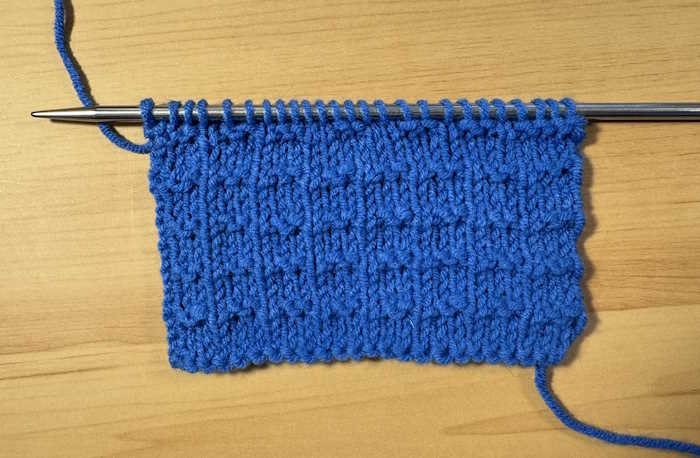 A swatch of the double andalusian stitch worked in blue yarn and still on the needle.