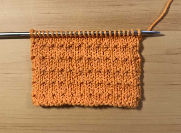 A swatch of the andalusian stitch worked in orange yarn and still on the needle