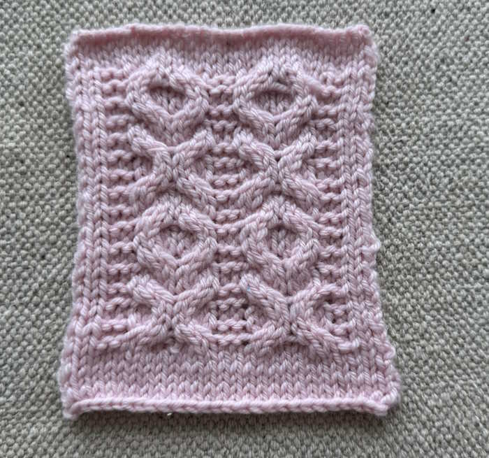 A swatch of the xoxo knit cable pattern worked in pink wool yarn A swatch of the xoxo knit cable pattern worked in pink wool yarn