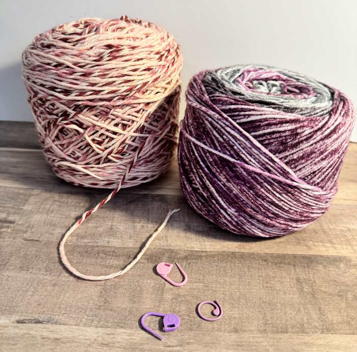 Two cakes of yarn are show with a couple of stitch markers Two cakes of yarn are show with a couple of stitch markers