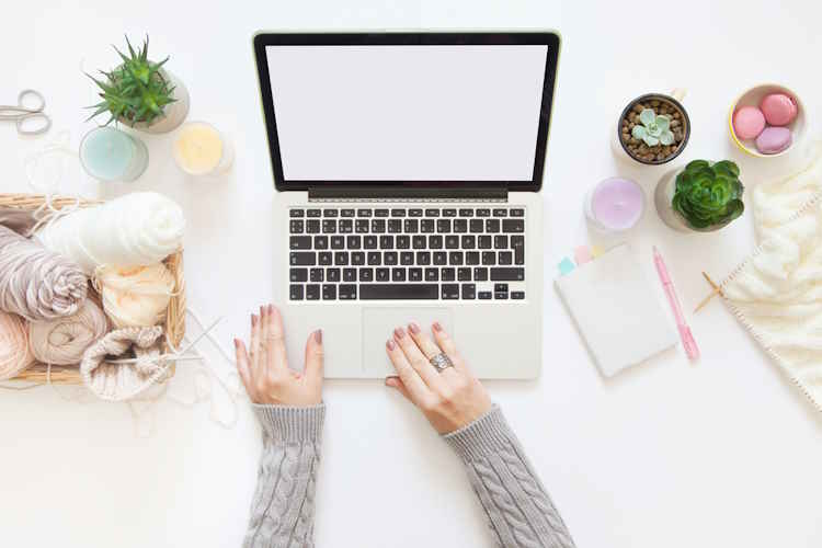 A woman is working at a laptop with knitting and yarn beside her A woman is working at a laptop with knitting and yarn beside her