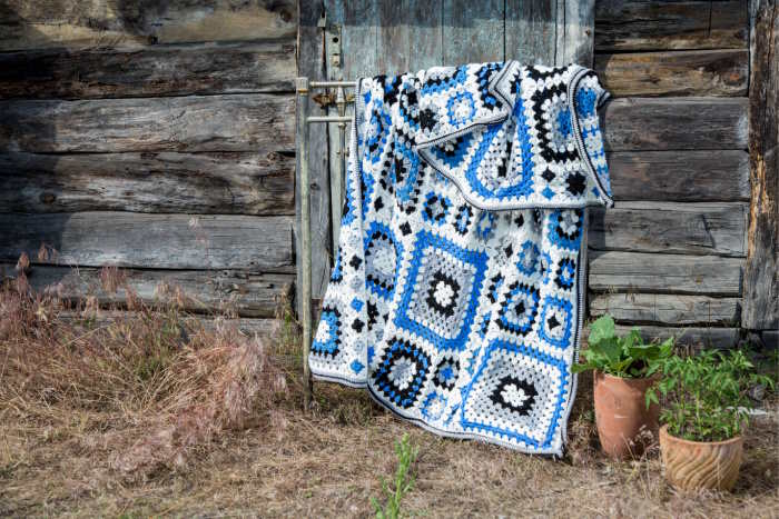 A blue, white, gray and black granny square blanket is hanging outside in a rural setting A blue, white, gray and black granny square blanket is hanging outside in a rural setting