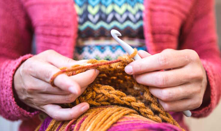 A woman is crocheting with a large hook, close up shot