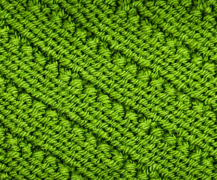 The wrong side of the diagonal seed stitch worked in green yarn.