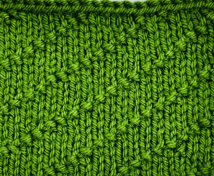 The right side showing of a knitted swatch of the diagonal seed stitch worked in green yarn The right side showing of a knitted swatch of the diagonal seed stitch worked in green yarn