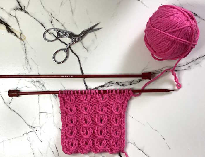 Eyelet Mock Cable Ribbing Stitch A swatch of the eyelet mock cable rib stitch worked in worsted  weight rose colored yarn.