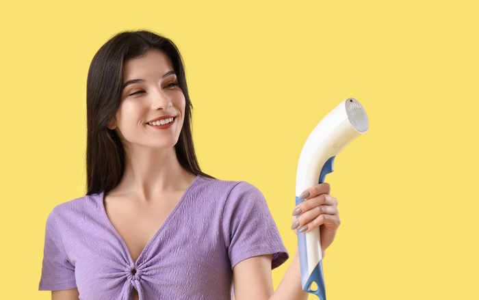 A young woman holding a spray fabric steamer in front of a yellow background
