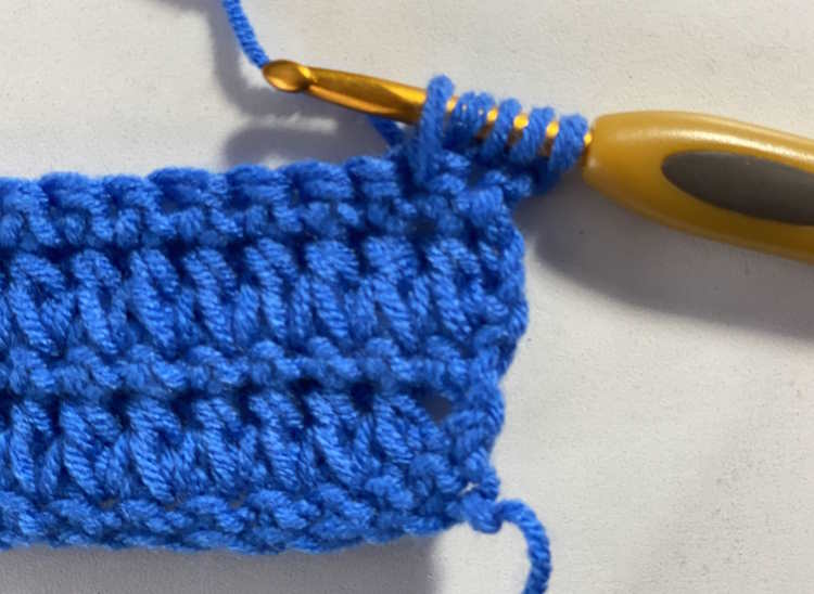 Part of a step by step tutorial showing how to make the forked half double crochet with 5 loops on the hook.