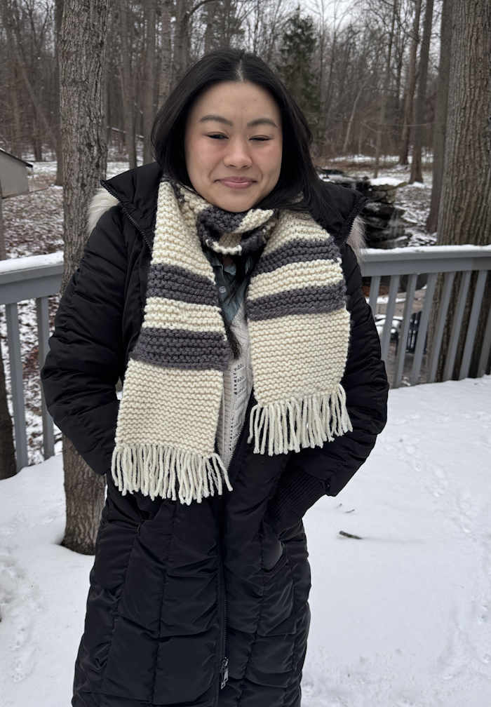 A gray and white striped garter stitch scarf modeled by a young woman