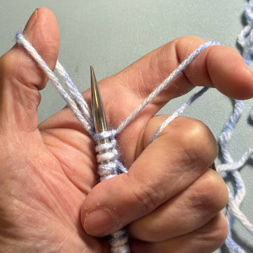 German twisted cast on being demonstrated with the sling shot position