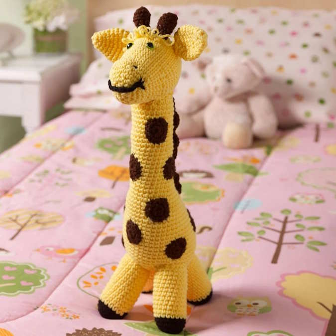 A toy crocheted giraffe sitting on a bed