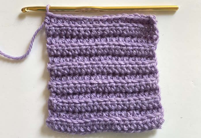 Ribbed half double crochet worked in back loops using purple yarn, showing knit-like ridges.