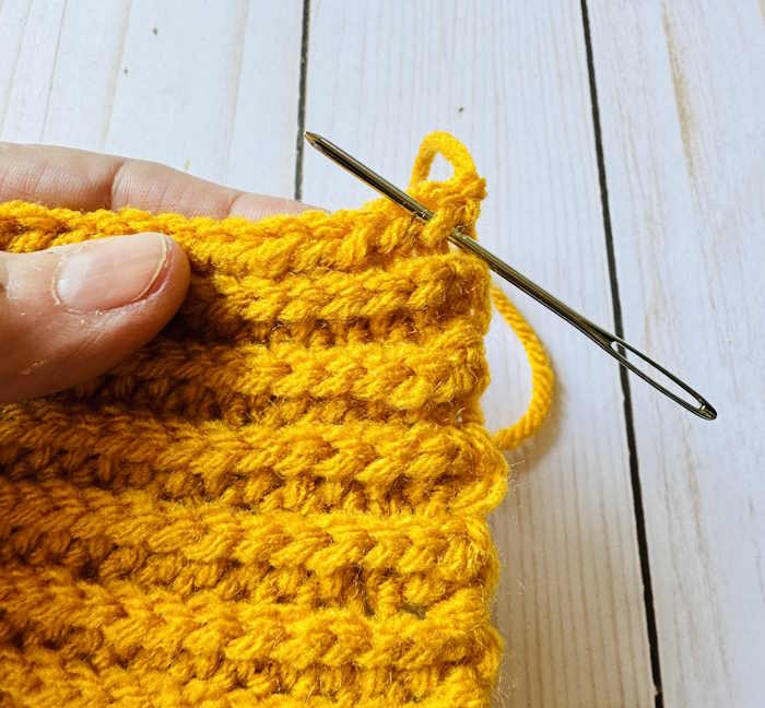 A tapestry needle is inserted in the third loop where the first stitch should be made when crocheting the half double crochet slip stitch ribbing