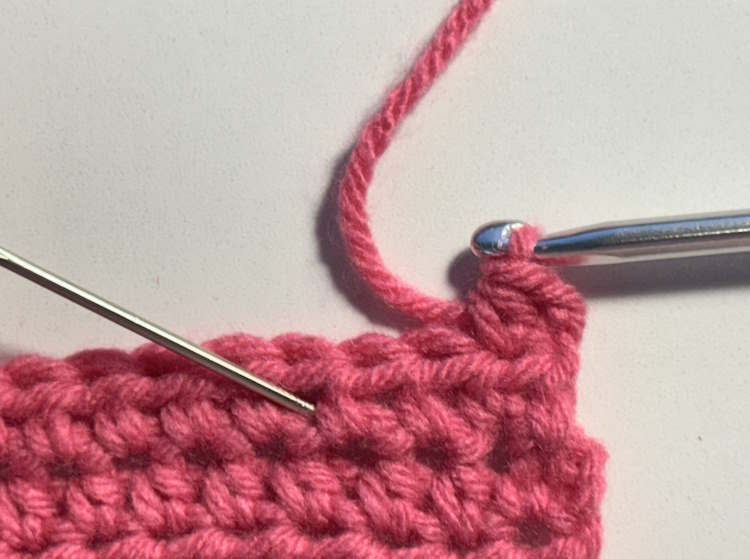 A half double crochet swatch marked with a yarn needle where to insert the hook when making a half double crochet offset stitch