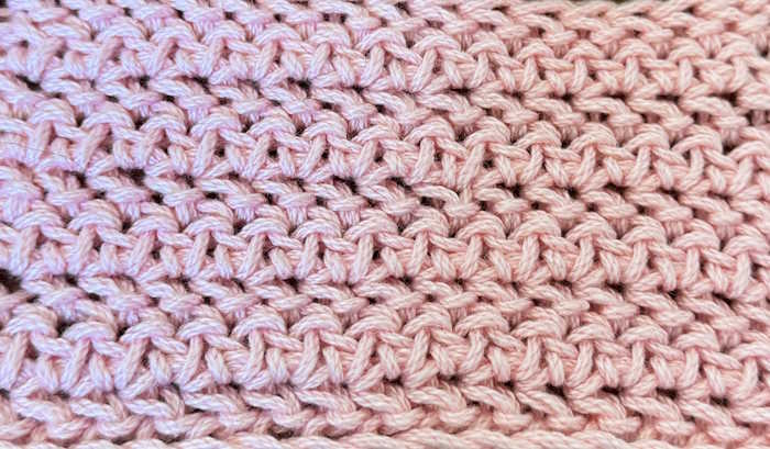 A closeup view of the herringbone half double crochet stitch pattern worked in pink cotton yarn