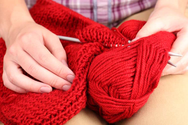 A project worked in red yarn shown with two human hands A project worked in red yarn shown with two human hands