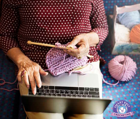 A woman with a laptop is holding knitting needles and yarn
