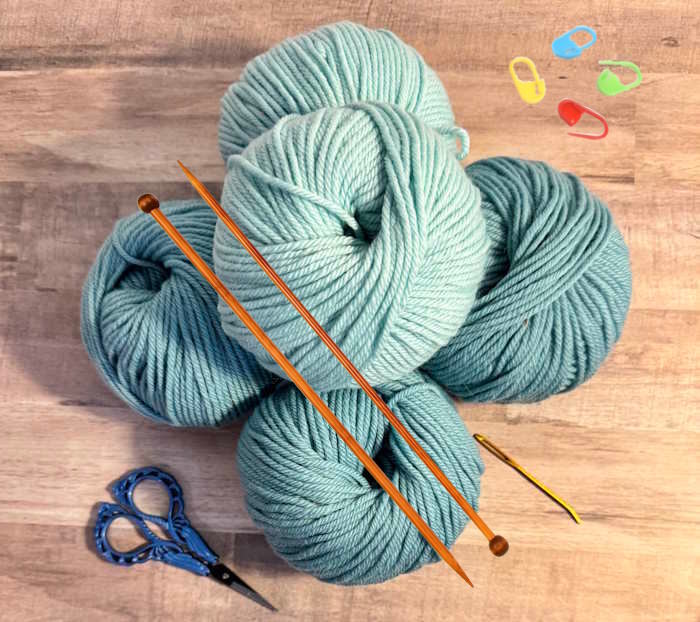 A knitting kit for beginners showing yarn, needles, scissors, and stitch markers