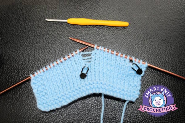 A swatch of knitting on needles showing a dropped stitch