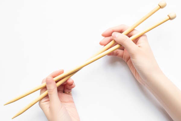 A set of bamboo straight knitting needles held by a person. A set of bamboo straight knitting needles held by a person.