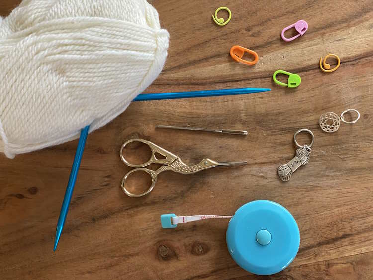 An assortment of knitting supplies including needles, yarn, scissors, tape measure and stitch marker An assortment of knitting supplies including needles, yarn, scissors, tape measure and stitch marker