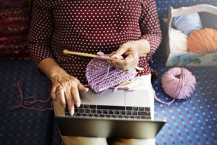 A woman is knitting while checking her laptop