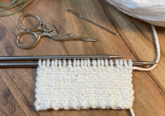 The Linen Knit Stitch pattern still on needles worked on a chunky acrylic yarn