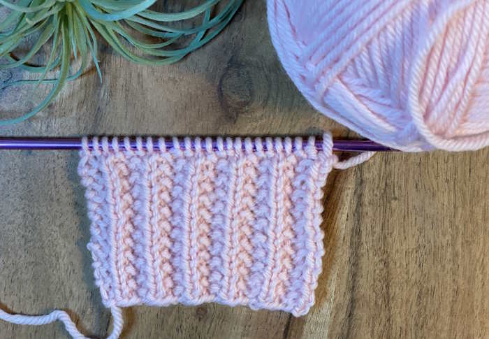 The Mistake rib knit chart worked in pink wool shown still on needles