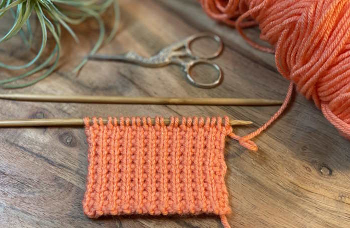 The Mock ribbing slip stitch pattern on the needles worked in an orange acrylic yarn