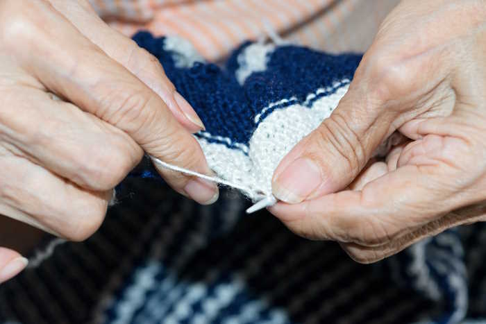 An older person is shown knitting a garter stitch swatch