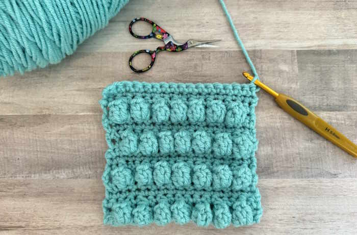 A swatch of the crochet popcorn stitch worked in teal 100% acrylic yarn