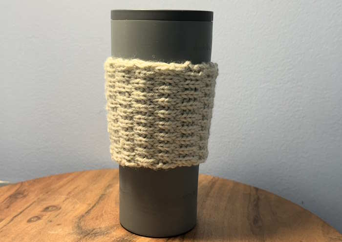 A cup cozy knit in the Roman knit rib stitch shown on a tall cup A cup cozy knit in the Roman knit rib stitch shown on a tall cup