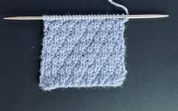 The seersucker knit stitch pattern worked in blue wool yarn