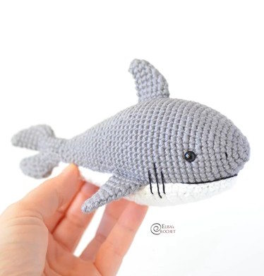 A small toy shark crocheted in gray and cream colored yarn