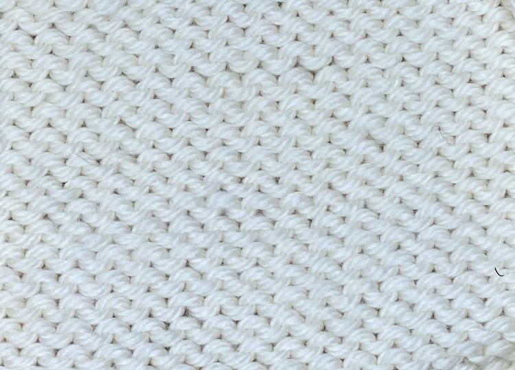 The reverse or wrong side of the stockinette stitch pattern worked in white wool yarn
