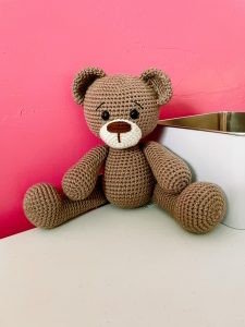 A toy teddy bear is crocheted in brown yarn