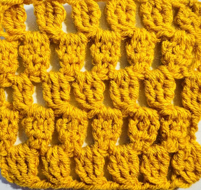 A swatch of the treble crochet cluster stitch worked in gold acrylic yarn A swatch of the treble crochet cluster stitch worked in gold acrylic yarn