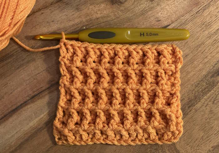 A swatch of the crochet waffle stitch shown worked in orange acrylic worsted weight yarn